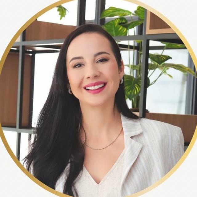 Tatiana Daré sorrindo, de blazer claro listrado, diante de uma estante com plantas